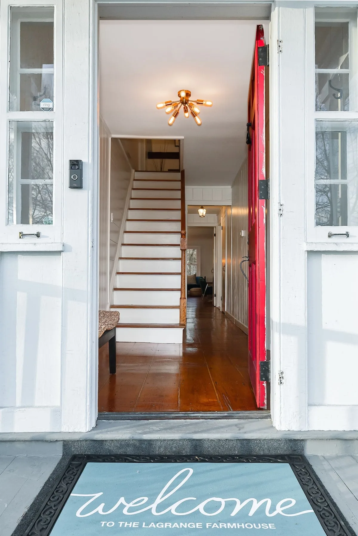 Open red front door and welcome mat at the farmhouse entry