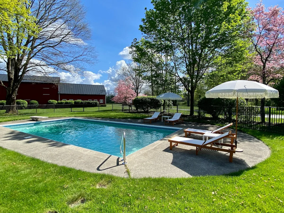 Seasonal in-ground swimming pool with loungers and red barn beyond