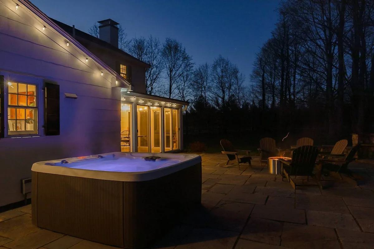 Five-person hot tub glowing beside the farmhouse at twilight